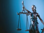 CFTC Sues Wisconsin in Escalating Fight Over Prediction Market Regulation A statue of Lady Justice holding scales in front of a blue background.