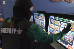Florida authorities bust Manatee County illegal gambling network during enforcement Florida sheriff investigator examines illegal gambling slot machines during Manatee County arcade enforcement raid and statewide Florida gaming crackdown