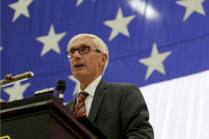 Gov. Evers bars Wisconsin employees from exploiting insider information through prediction markets Wisconsin Governor Evers speaking at podium with American flag backdrop addressing tribal mobile sports betting legislation. Gov. Evers bars Wisconsin employees from exploiting insider information through prediction markets