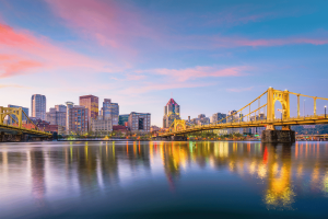 Pennsylvania regulators approve $180K in gaming fines while expanding involuntary Pittsburgh skyline at sunset with illuminated yellow bridges reflecting across the Allegheny River in downtown Pennsylvania. Pennsylvania regulators approve $180K in gaming fines while expanding involuntary exclusion lists