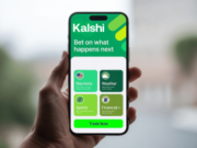 BBB refers Kalshi in advertising inquiry after company declines review participation Hand holding a smartphone displaying the Kalshi prediction market platform with election, weather, sports and financial forecasting markets. BBB refers Kalshi in advertising inquiry after company declines review participation